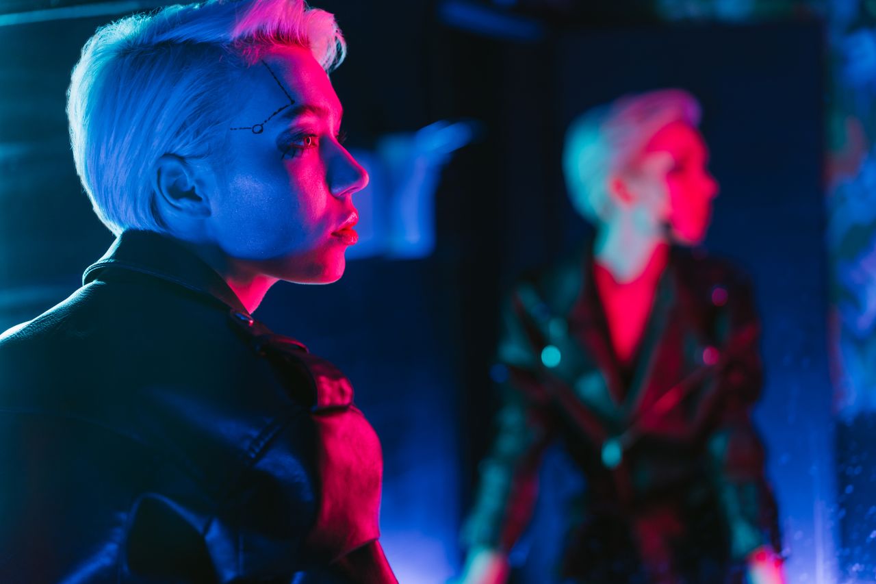 A woman in a black leather jacket poses with vivid neon lights and reflection.